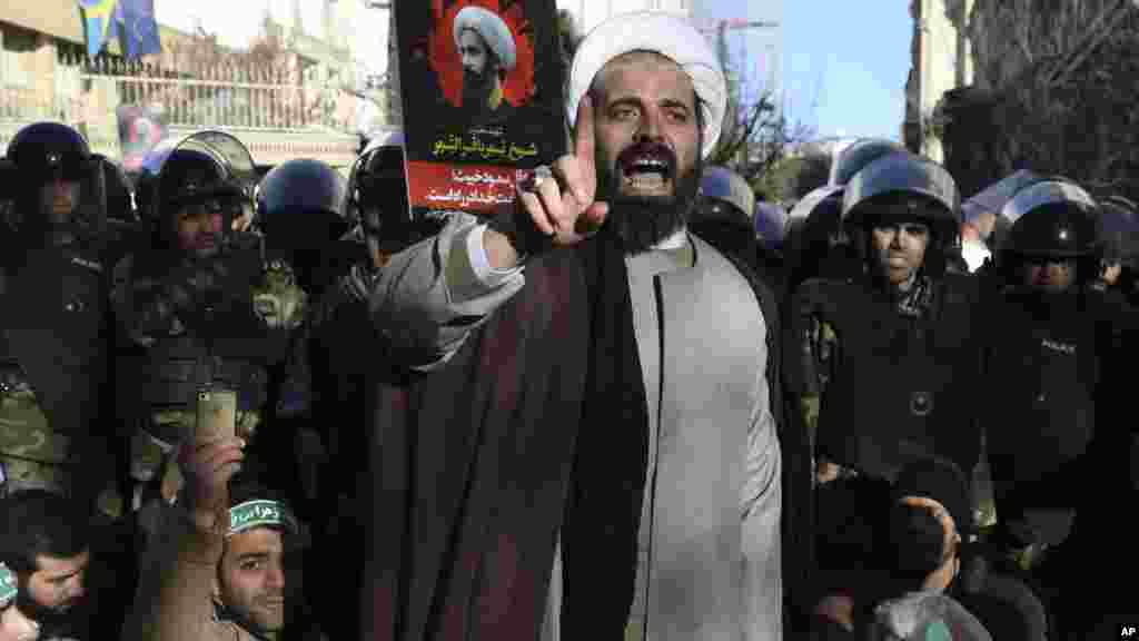 Malamin 'Yan Shi'a Kewaye Da Jami'an Tsaro Na Huduba Ga Jma'ar Sa A Lokacin Da Suke Gudanar Da Zangazangar Nuna Kin Jinin Kinsan Da Gwamnatin Kasar Saudiyya Ta Yi Ma Wani Malamin 'Yan Shi'a A Kofar Ofishin Jakadancin Saudiyya Da Ke Birnin Tehran Na Kasar Iran Janairu 4, 2016 