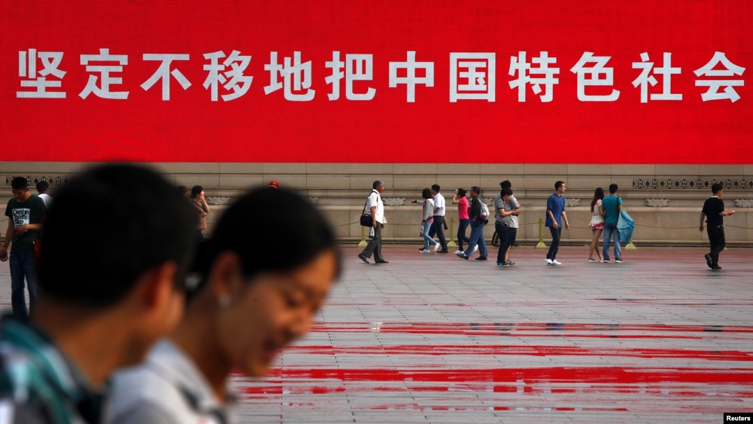 人們走過北京天安門廣場豎立的一幅宣傳中國特色社會主義道路的巨幅標語。 （2012年6月3日）