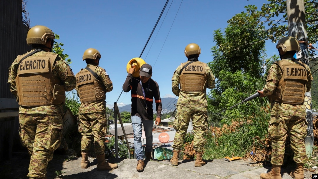 ARCHIVO - Un hombre transporta propano junto a soldados en el barrio 10 de Octubre durante un despliegue gubernamental de soldados y policías para reprimir las pandillas en San Marcos, El Salvador, el lunes 28 de octubre de 2024. AP