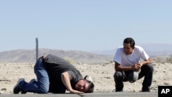 Ron Mikulaco, a la izquierda, se agacha para ver una grieta causada por un terremoto junto a su sobrino Brad Fernández en la carretera 178 el sábado 6 de julio de 2019, en las afueras de Ridgecrest, California.
