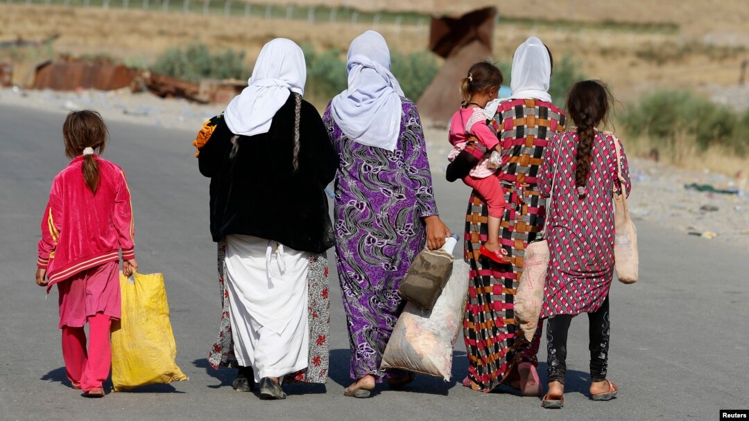 FILE - Women and children from the minority Yazidi sect, fleeing the violence in the Iraqi town of Sinjar, walk to a refugee camp after they re-entered Iraq from Syria at the Iraqi-Syrian border crossing in Fishkhabour, Dohuk province, Aug. 14, 2014.