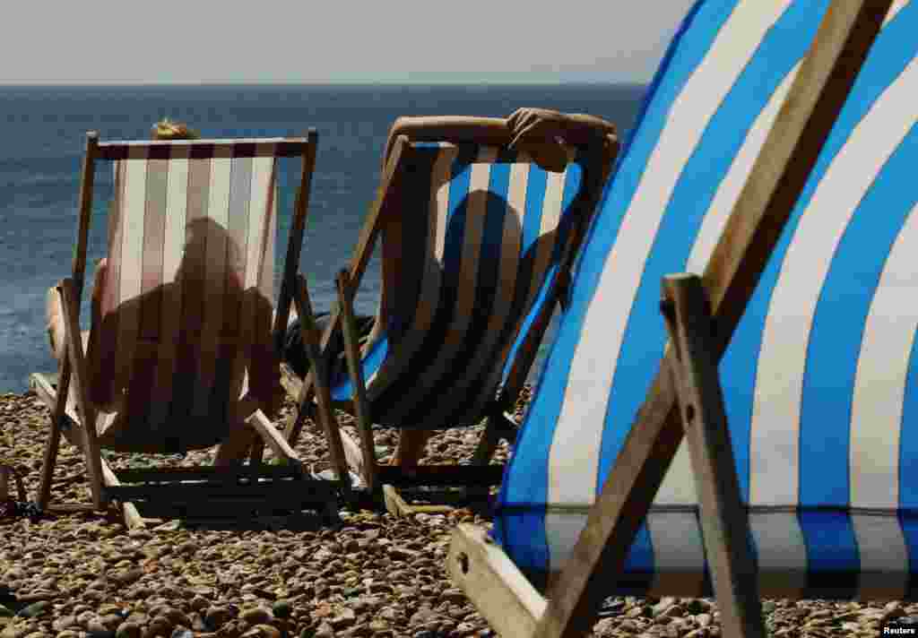 A couple sunbath in deck chairs on Brighton Beach, southern England. Britain's first prolonged heatwave in seven years has taken the country by surprise, with rails buckling, shops selling out of electric fans, and scientists estimating the surge in temperature could have caused hundreds of premature deaths.