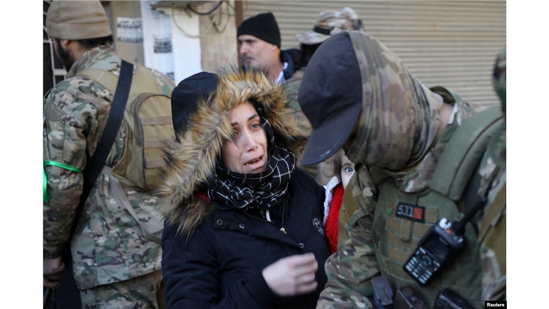 A woman reacts near fighters of Hayat Tahrir al-Sham during what HTS said were security checks to find "remnants" of ousted Syrian President Bashar al-Assad's force, in Wadi al-Dahab neighborhood in Homs, Syria, Jan. 2, 2025.