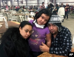 FILE - Wildfire survivors Marolyn Romero-Sim, left, with Hugo Romero-Rodriguez, middle, and their 9-year-old daughter, Milagros, sit inside the evacuation center at the Ventura County Fairgrounds in Ventura, Calif. Their RV burned up with all their possessions.