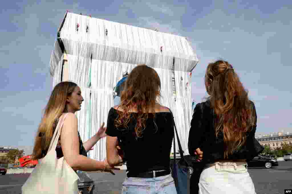 Bystanders look on as workers arrange silver blue fabric, part of a process of wrapping L'Arc de Triomphe in Paris, France, designed by the late artist Christo.