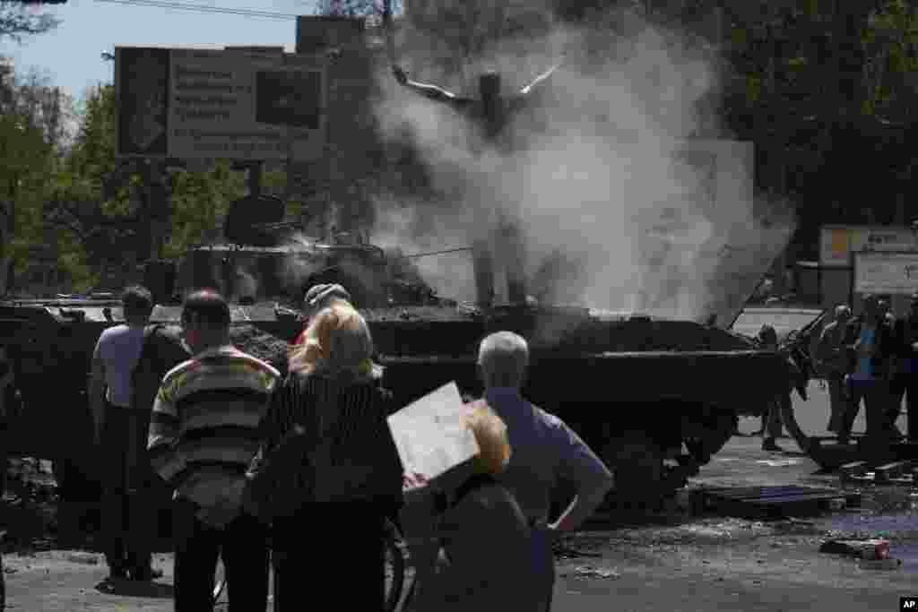 People watch as a seized armored vehicle that was set on fire smolders in the center of Mariupol, eastern Ukraine, May 10, 2014.