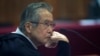 ARCHIVO - El expresidente peruano Alberto Fujimori, encarcelado, fotografiado a través de una ventana de vidrio, asiste a su juicio en una base policial en las afueras de Lima, Perú, el 28 de junio de 2016.