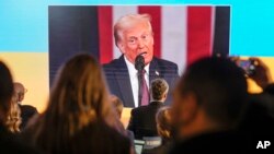 Varias personas siguen la toma de posesión de Donald Trump en pantallas en la casa de Ucrania, en el Foro Económico Mundial, en Davos, Suiza, el 20 de enero de 2025.