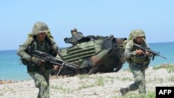 Philippine marines take position next to US Marines Amphibious Assault Vehicles (AAV) during an amphibious landing exercise at the beach of the Philippine navy training center facing the South China Sea in San Antonio town, Zambales province, north of Man