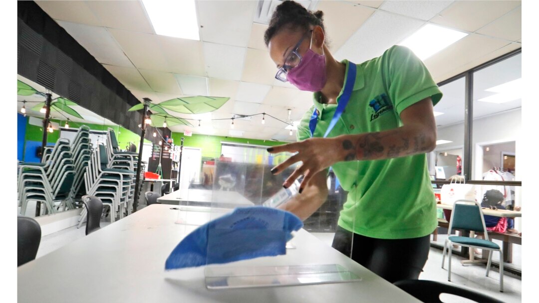 Camp counselor Mia Porche wipes down plastic barriers used to distance children during lunch at a daycare summer camp in Richardson, Texas, Tuesday, May 19, 2020.