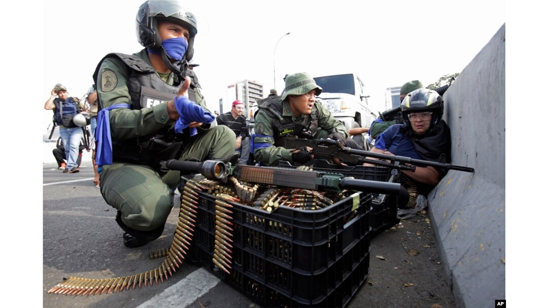 An anti-government protester, right, takes cover amid rebel troops who are rising up against the government of Venezuela's President Nicolas Maduro, on an overpass outside La Carlota military airbase as they confront loyal troops at the base.