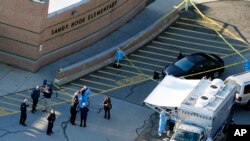 FILE - Officials stand outside of Sandy Hook Elementary School in Newtown, Conn., where authorities gunman Adam Lanza opened fire inside the school killing 20 first-graders and six educators at the school and killed himself as police arrived.