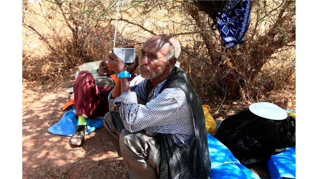 FILE - An Ethiopian refugee who fled fighting in Tigray province sits holding a radio in the shade of a straw shack at the Um Rakouba camp in Sudan, Nov. 18, 2020.