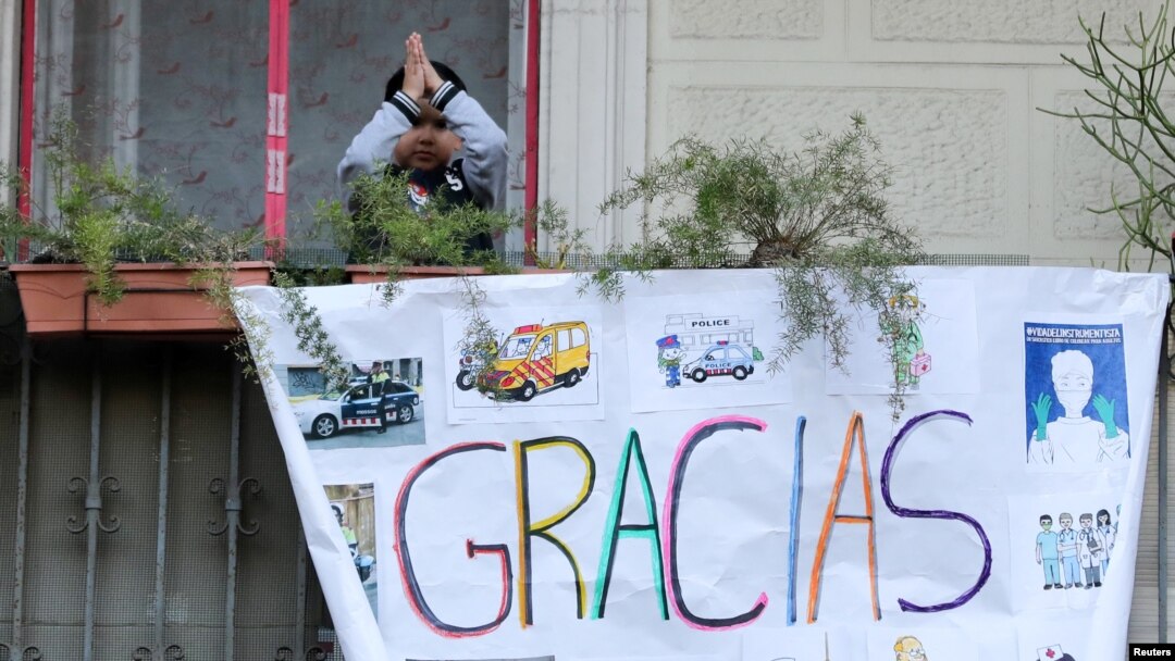 Un niño saluda desde un balcón en Barcelona, España, detrás de un cartel de apoyo a los trabajadores de la salud que luchan contra el coronavirus, el 11 de abril de 2020.