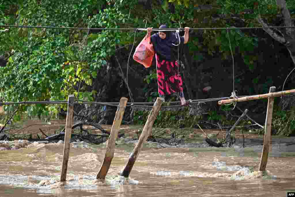A woman crosses a river using the remains of a bridge, swept away during last year's flooding, at Malela village in Luwu Regency, South Sulawesi, Indonesia.