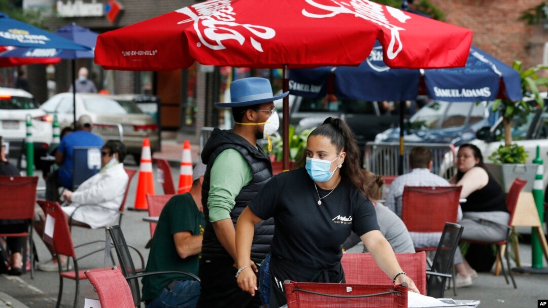 A waitress seats customers at a restaurant with outdoor dining on a section of street closed to traffic to promote social distancing, July 17, 2020, in Somerville, Mass.