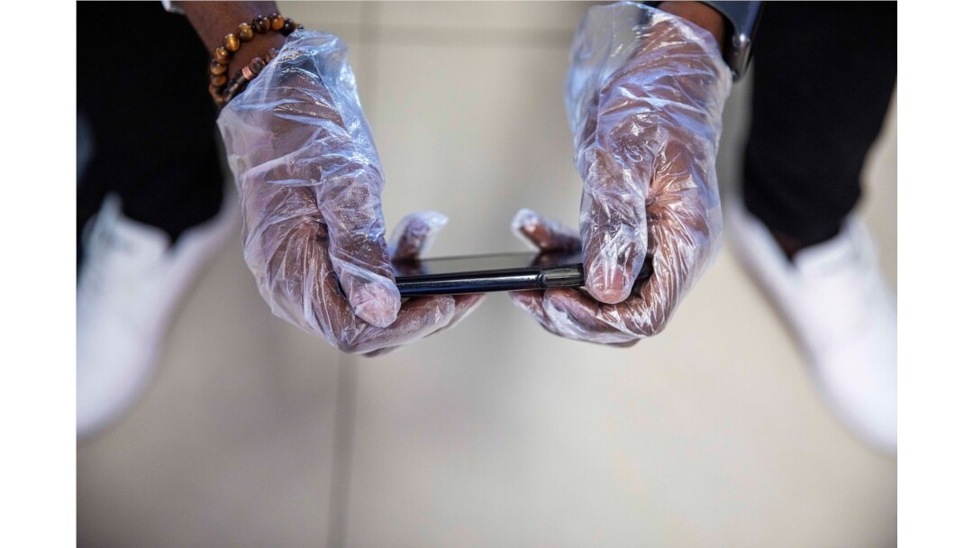 A passenger wears gloves to use his phone while waiting to board a flight at Toussaint Louverture International Airport, March 14, 2020, in Port-au-Prince, Haiti. As of Saturday, there were no reported cases of COVID-19 in Haiti.