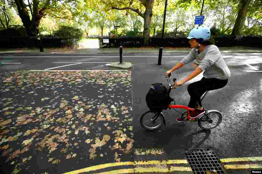 A woman cycles her bike along a road, where the fallen autumn leaves have made a pattern, in central London, Oct. 13, 2018.