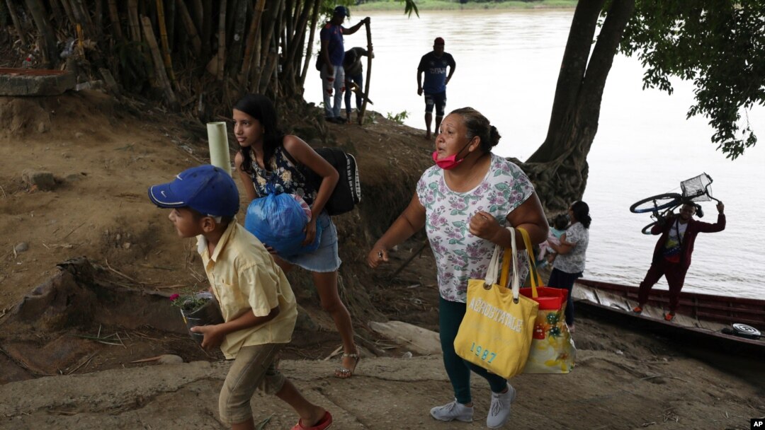 Una familia venezolana lleva sus pertenencias luego de cruzar el río Arauca en bote para salir de Venezuela, en Arauquita, Colombia. Marzo 25, 2021. Foto: AP.