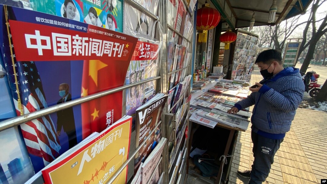 FILE - A newsstand vendor looks through his display near a magazine with a cover depicting U.S. President Joe Biden near U.S. and Chinese flags in Beijing on Jan. 21, 2021.