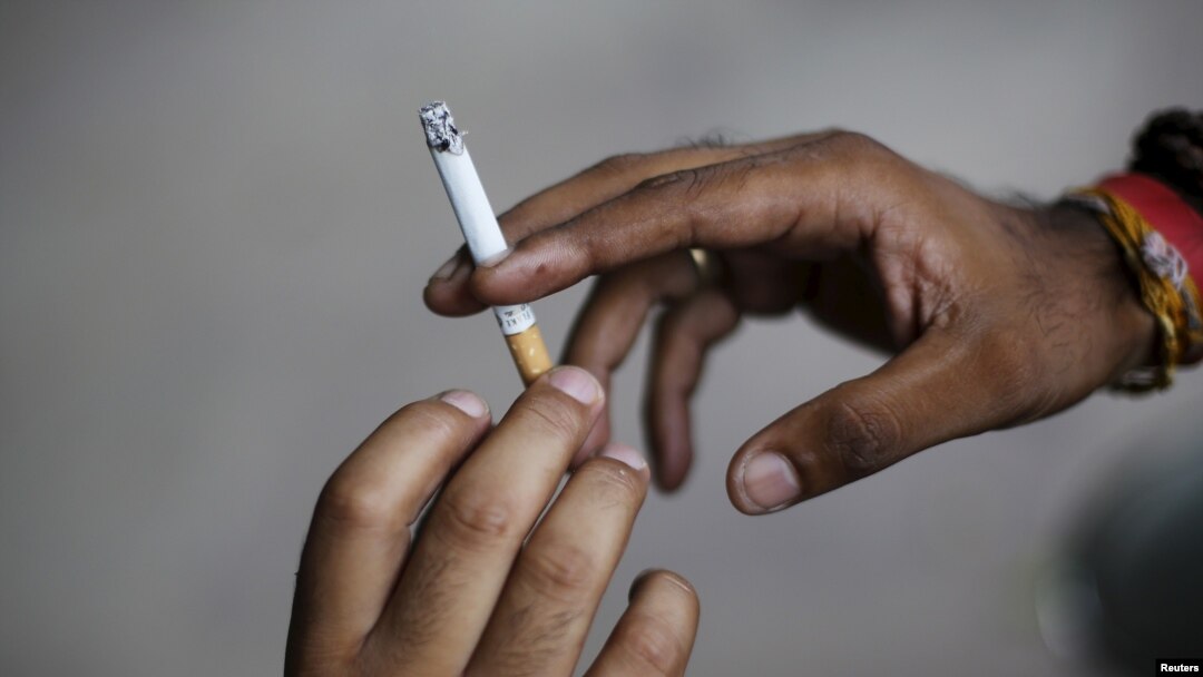 FILE - A man passes a cigarette to another as they sit on a pavement along a road in New Delhi, India, Aug. 18, 2015. 