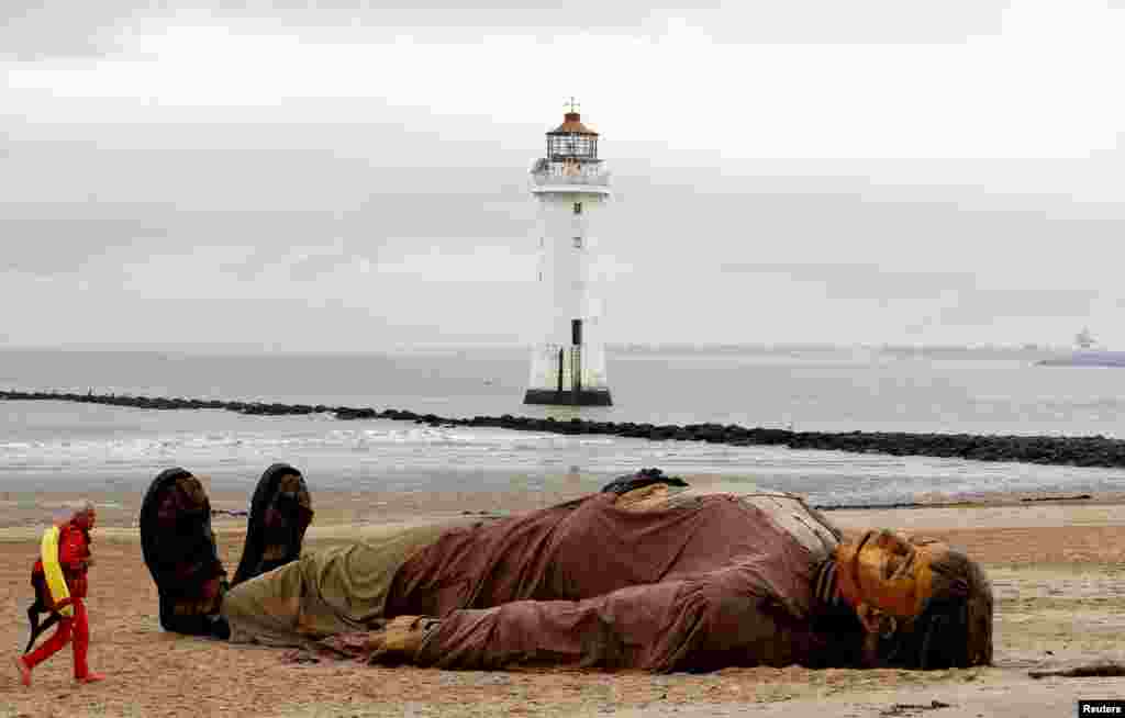A lifeguard passes one of Royal Deluxe's giant marionette puppets as it lies on the beach at New Brighton, Britain.