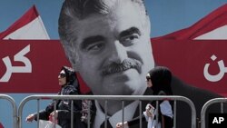 Lebanese women pass by a giant portrait of slain Lebanese Prime Minister Rafik Hariri near his grave, in downtown Beirut, June 30, 2011