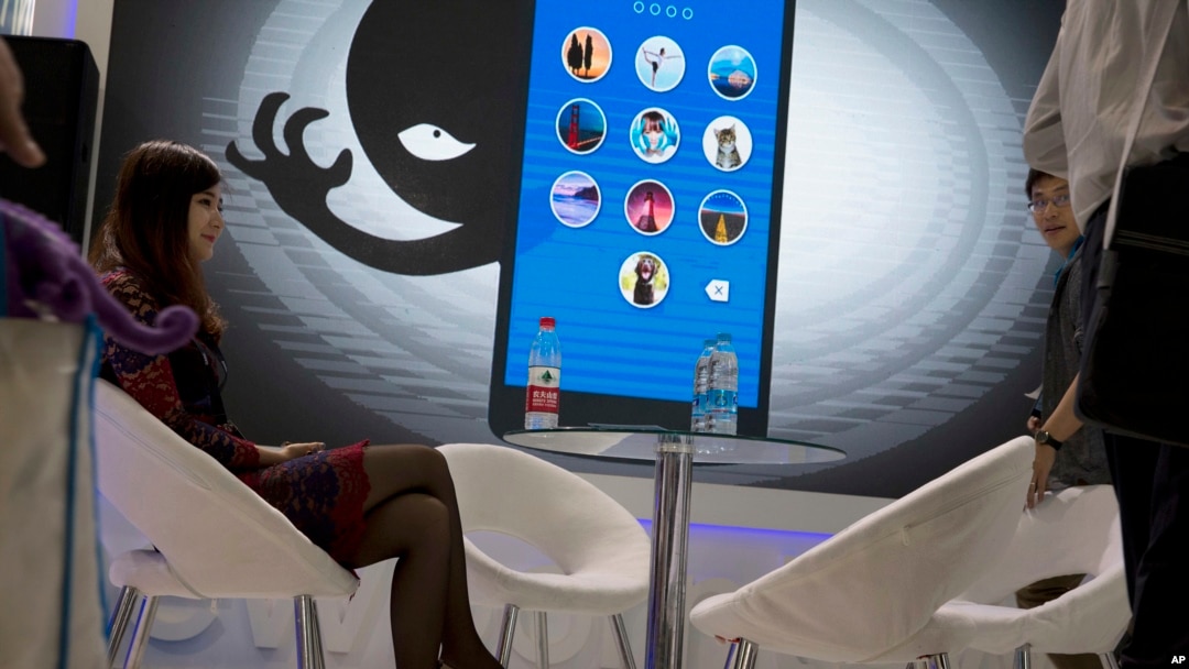 FILE - A woman sits near a display showing the dangers of hackers breaking into mobile devices during the Global Mobile Internet Conference in Beijing, China, April 29, 2016.