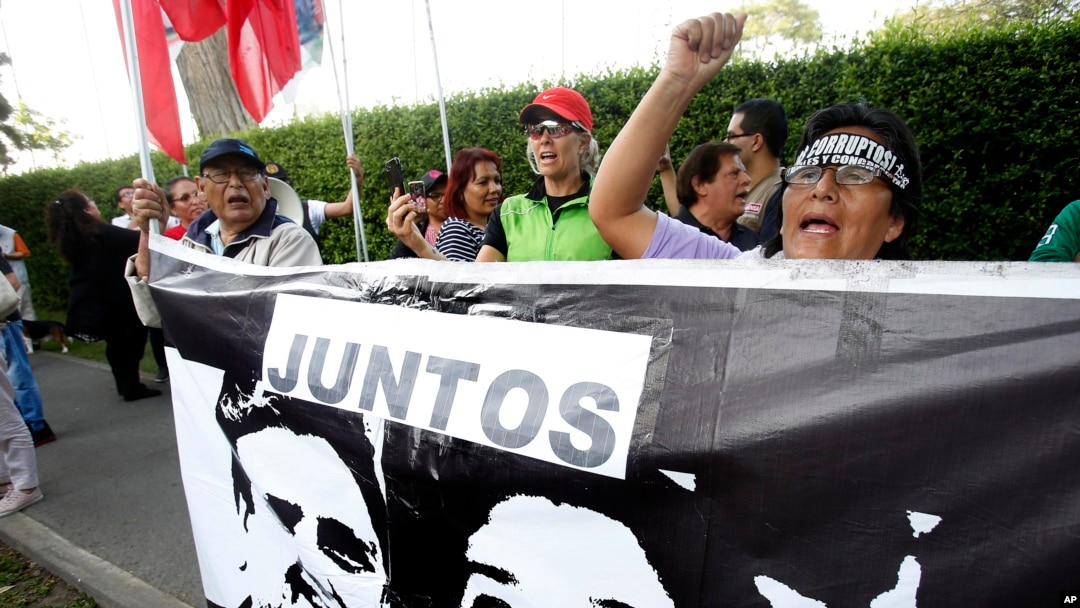 A woman shouts slogans against Peru's former president Alan Garcia outside the residence of Uruguay's ambassador to Peru, behind a sign showing an image of Garcia and Keiko Fujimori, in Lima, Peru, Nov. 18, 2018.
