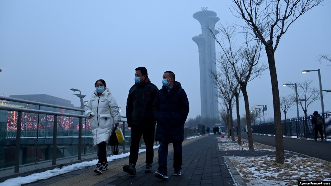 People walk along a path as the Beijing Olympic Tower is seen during a smoggy day in Beijing, Jan. 24, 2022. 