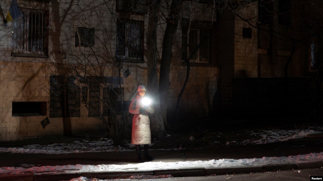 A woman holds a torch as she stands in a dark street during partial power cuts following a Russian attack on Ukrainian energy facilities, amid Russia's attack on Ukraine, in central Kyiv, Ukraine, Dec. 13, 2024.