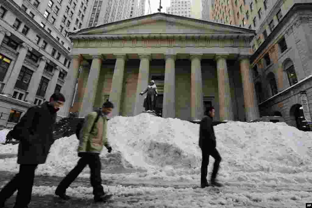 Morning commuters pass a pile of snow on Wall Street in New York's Financial District, Jan. 25, 2016.
