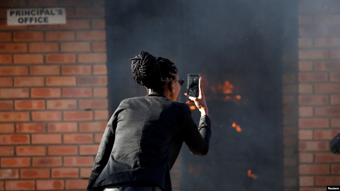 FILE - A women uses a cellphone to take pictures of a burning principal's school office in Mashau Dolly village in South Africa's northern Limpopo province, May 5, 2016. 
