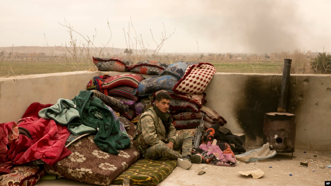 A U.S.-backed Syrian Democratic Forces (SDF) soldier sits on a rooftop as smoke rises from the battle to oust Islamic State militants from Baghuz, Syria, March 13, 2019. 