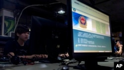 FILE - Computer users sit near a monitor display with a message from the Chinese government on the proper use of the Internet at an Internet cafe in Beijing, China, Aug. 19, 2013.