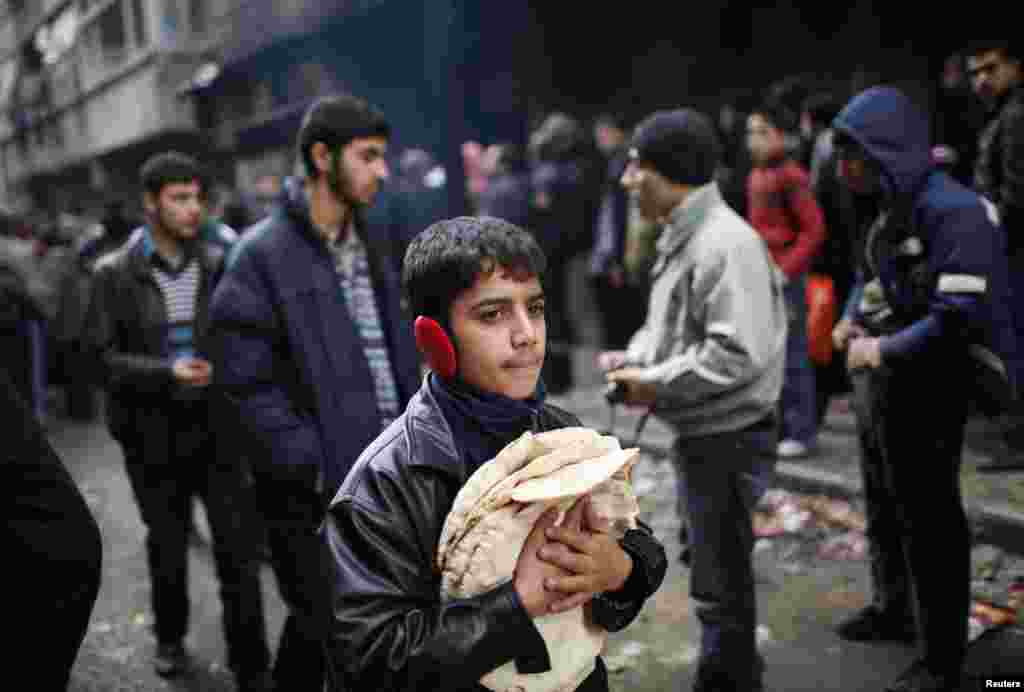 A boy holds pita bread as others stand in line outside a bakery in Aleppo, Syria, December 21, 2012.