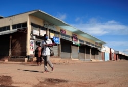 FILE - A man wears a mask as he walks past closed shops during a lockdown aimed at limiting the spread of the coronavirus disease (COVID-19) in Harare, Zimbabwe, Jan. 28, 2021.