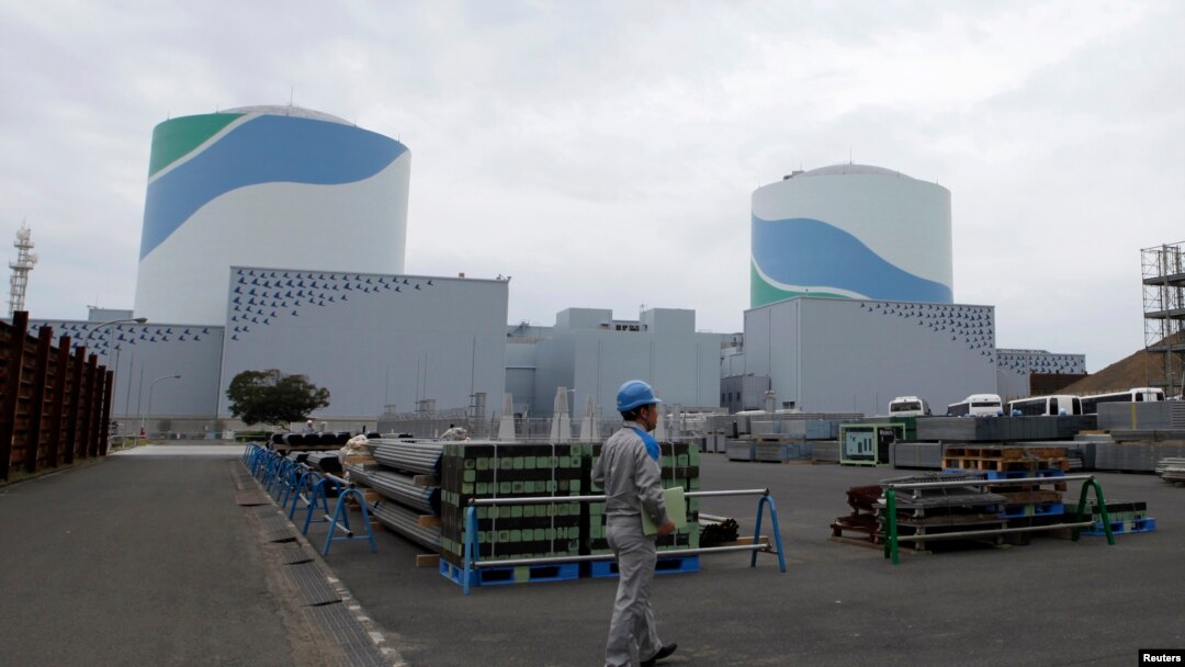 FILE - An employee of Kyushu Electric Power Co walks in front of reactor buildings at the company's Sendai nuclear power plant in Satsumasendai, Kagoshima prefecture.