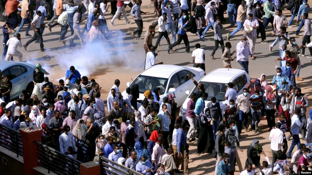 FILE - Demonstrators run from tear gas lobbed to disperse them as they march along the street during anti-government protests in Khartoum, Sudan, Dec. 25, 2018. 