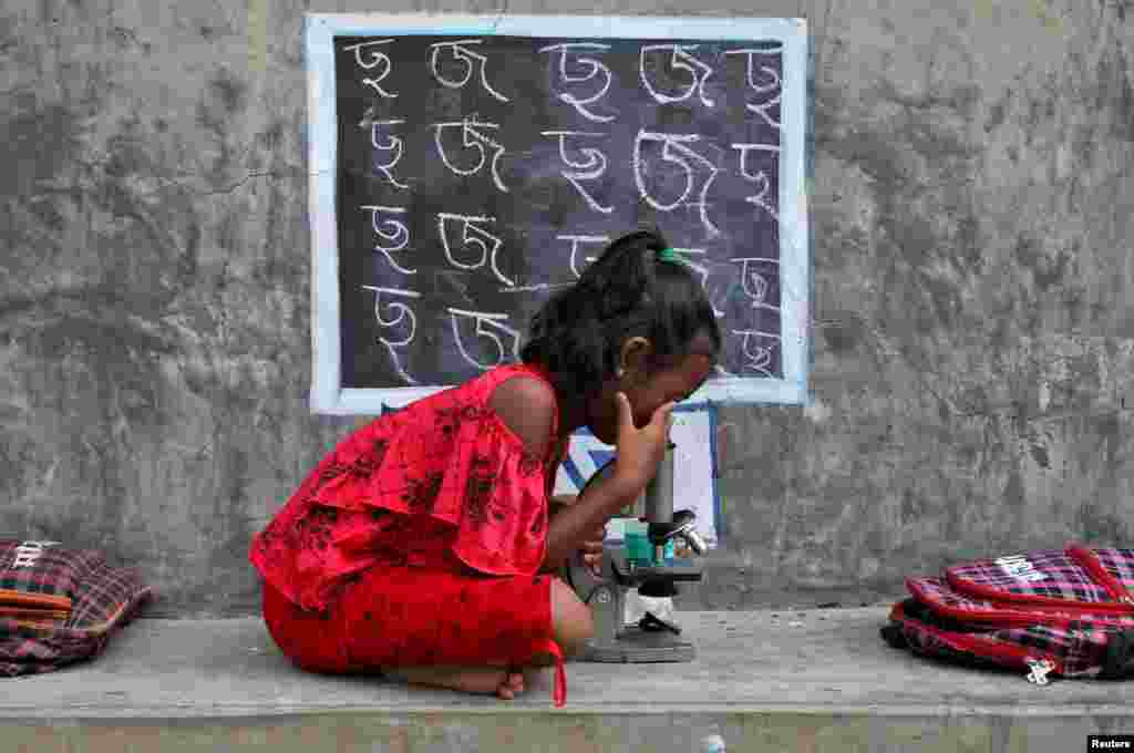 A girl, who does not have access to internet facilities and gadgets, uses a microscope as she attends an open-air class outside a house with its walls converted into black boards following the closure of their schools due to the COVID-19 outbreak, at Joba Attpara village in Paschim Bardhaman district in the eastern state of West Bengal, India, 